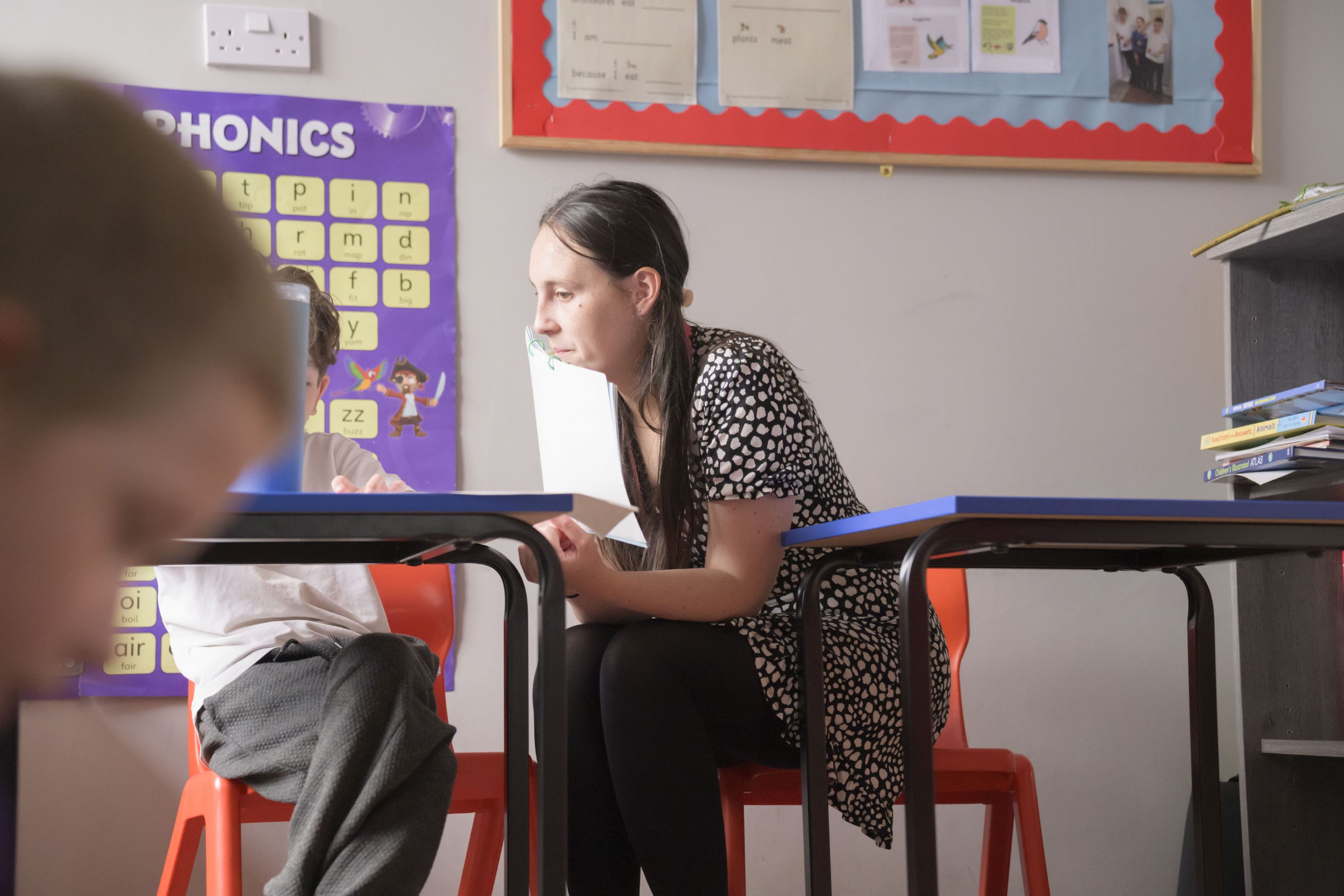 Image of carer looking at child reading a book